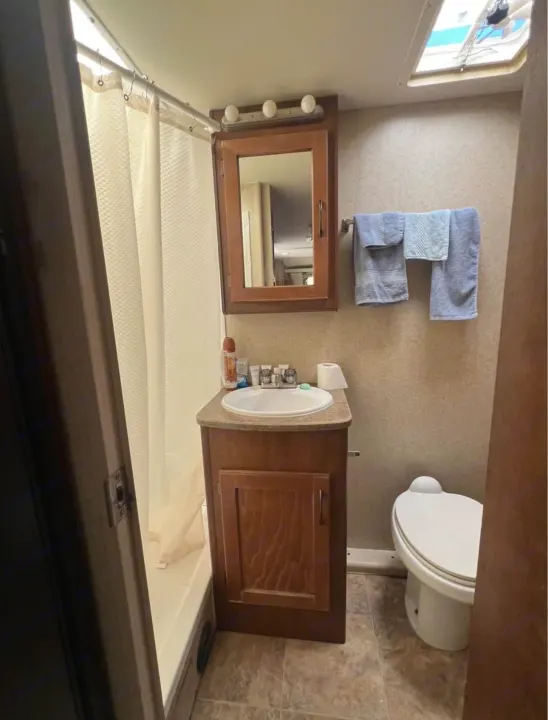 Compact RV rental bathroom, featuring a shower with curtain, vanity with sink, toilet, and mirror cabinet.. Lance Manufacturing Lance Manufacturing Trailer 2016