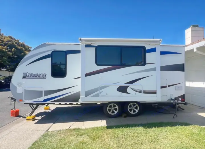 Find your perfect rv rental! A white Lance travel trailer with an extended slide-out, parked on a driveway.. Lance Manufacturing Lance Manufacturing Trailer 2016