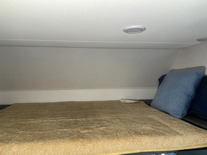 Cozy RV rental bunk bed with a light brown blanket, blue pillows, and recessed overhead lighting in a compact sleeping area.. Forester LE 2026