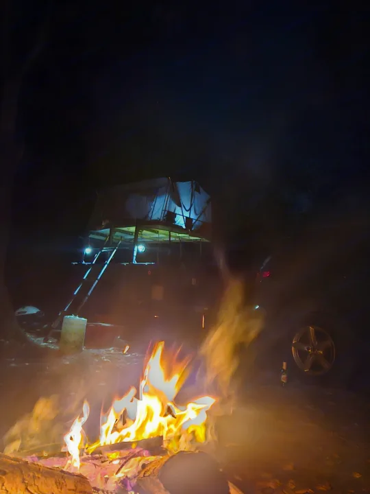Enjoying an RV rental adventure: a warm campfire glows next to a vehicle with a rooftop tent and ladder under the night sky.. Silver Eagle Manufacturing M1102 2013