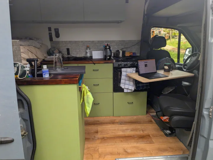 Inside a versatile RV rental camper van, featuring a compact kitchen, cozy bed, and a convenient laptop workspace.. Mercedes-Benz Sprinter 2014