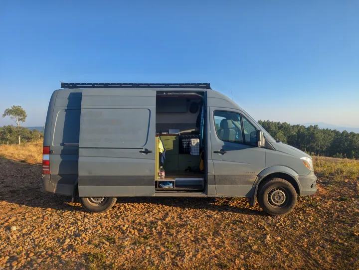 This gray Sprinter camper van, an ideal **rv rental**, is parked outdoors with its doors open, revealing a cozy interior.. Mercedes-Benz Sprinter 2014