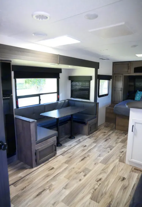 Bright RV rental interior featuring a modern dining area, sleek wood-look flooring, and a comfortable bed setup.. Venture Venture Trailer 2023