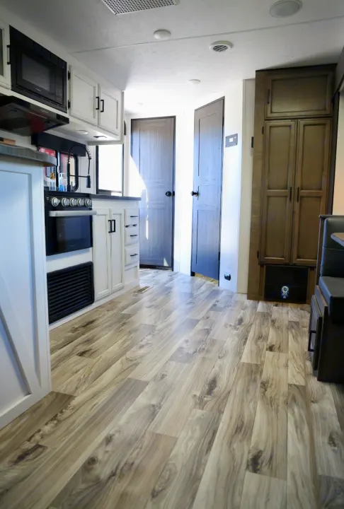 Bright RV rental interior with a modern kitchen, white cabinets, light wood-look flooring, and a glimpse of the dinette.. Venture Venture Trailer 2023