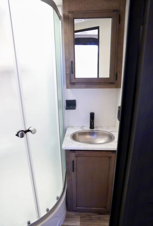 An RV rental's small bathroom: frosted shower, vanity with a steel sink, and a wooden medicine cabinet.. Venture Venture Trailer 2023