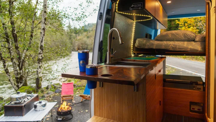 Cozy RV rental interior with kitchen, bed, and river view. Perfect for outdoor cooking by the campfire!. Mercedes Sprinter 2017