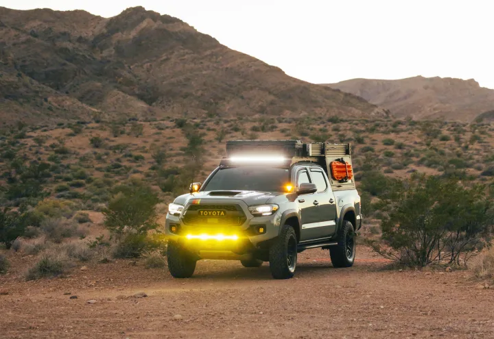 Rugged Toyota Tacoma overlanding truck with bright lights in desert mountains. Explore with this unique RV rental!. Toyota Tacoma 2021