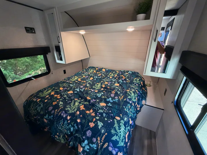 Inside an RV rental: A cozy bedroom featuring a floral bedspread, overhead cabinets with lighting, and windows for natural light.. Jayco Jay Flight 284BH 2025