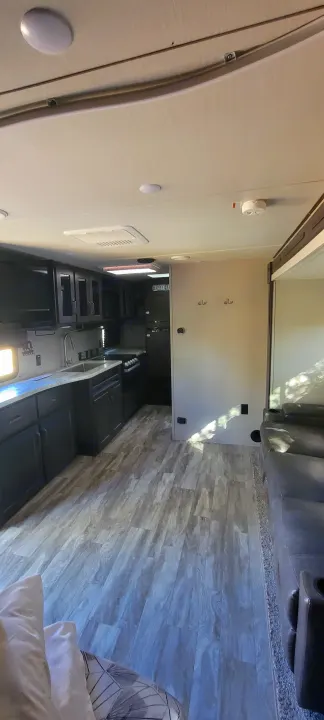 Modern RV rental interior: a sleek kitchen with dark cabinets, a cozy living area, and light wood-look flooring.. Grand Design Transcend Xplor 2022