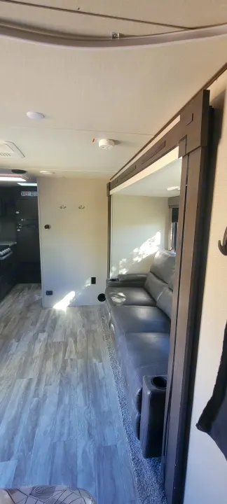 Explore this bright RV rental interior: a comfy grey sofa in a slide-out, wood-look floor, and functional kitchen area.. Grand Design Transcend Xplor 2022