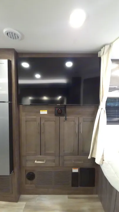 RV rental interior features: wall-mounted TV, storage cabinets, refrigerator, and ceiling vent, creating a functional living space.. Entegra Coach Odyssey 25R 2026