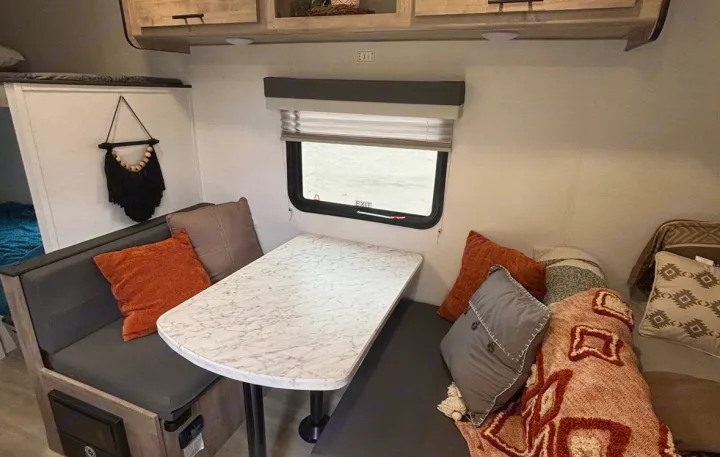 Cozy RV rental dinette area with comfy seating, a central table, and window, adorned with pillows.. Gulf Stream Enlighten Super Lite 2025