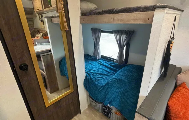 RV rental: Cozy bunk beds with a window, dressed in a blue blanket, beside a door with a full-length mirror.. Gulf Stream Enlighten Super Lite 2025