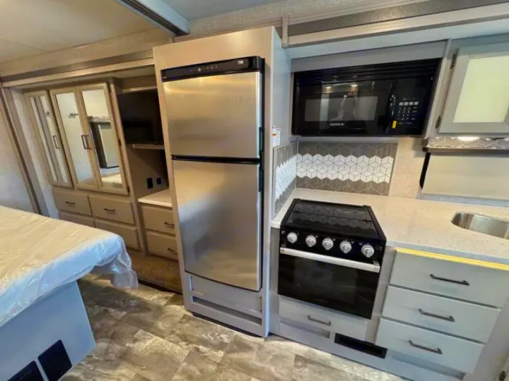 RV rental interior: modern kitchen with stainless fridge, microwave, stove, sink, and adjacent bedroom wardrobe with TV.. Thor Windsport 2023