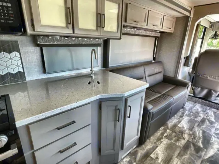 Modern RV rental interior with compact kitchen, sink, and sofa seating area. Gray tones, perfect for travel.. Thor Windsport 2023