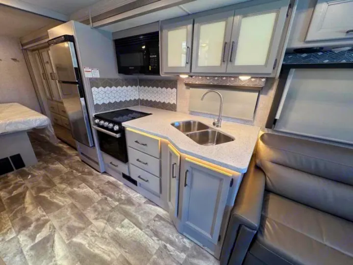 RV rental interior: a functional kitchen with stove, sink, and fridge, connecting to the sleeping and living areas.. Thor Windsport 2023