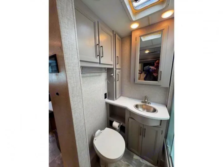 Modern RV rental bathroom, featuring a white toilet, sink vanity, mirrored cabinet, and overhead storage for convenience.. Thor Windsport 2023