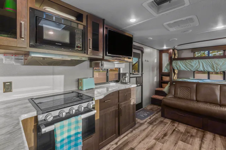 Spacious RV rental interior with a fully equipped kitchen, cozy sofa, and bunk beds, ideal for travel adventures.. Grand Design Transcend Xplor 2023