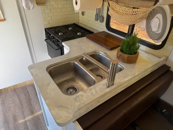 RV rental kitchen features a double sink, gas stove, light countertops, subway tile, and a built-in dining bench.. Itasca Spirit 1996