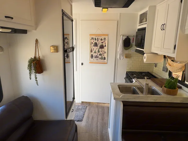 Inside an RV rental: a compact kitchen with sink, stove, and microwave, plus a comfy living area with a dark couch.. Itasca Spirit 1996