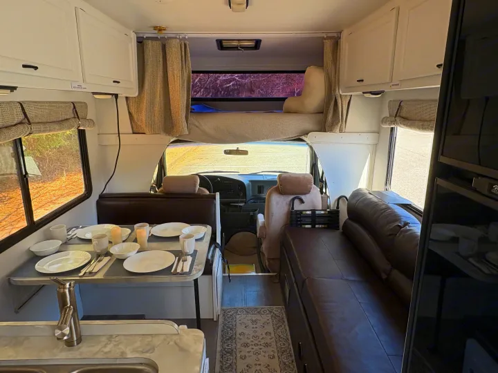 Bright and cozy rv rental interior shows dining, kitchen area with sink, seating, and over-cab bed.. Itasca Spirit 1996