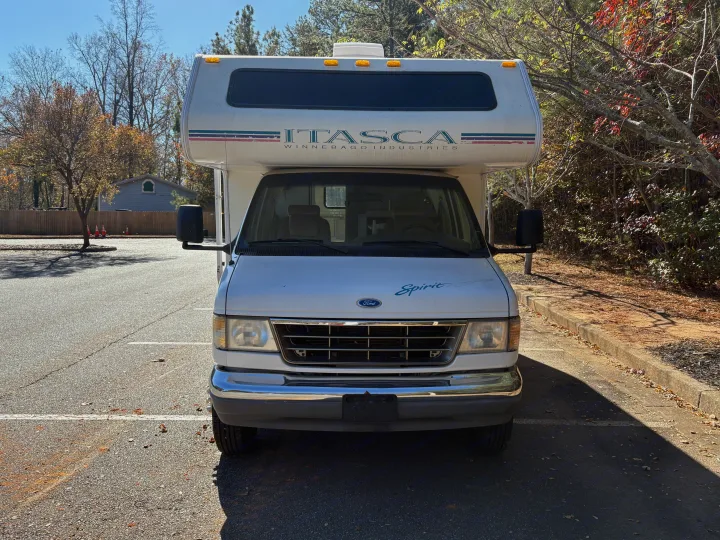 Front view of a white Itasca Winnebago Spirit RV rental parked in an asphalt lot on a sunny day, showcasing its classic design.. Itasca Spirit 1996
