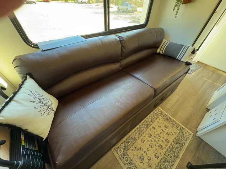 RV rental: Comfortable brown leather sofa with pillows, large window view, and a rug on wood flooring inside an RV.. Itasca Spirit 1996