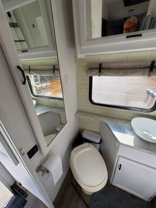 Clean RV rental bathroom featuring a toilet, vessel sink, subway tile backsplash, and window. An amenity list is on the wall.. Itasca Spirit 1996