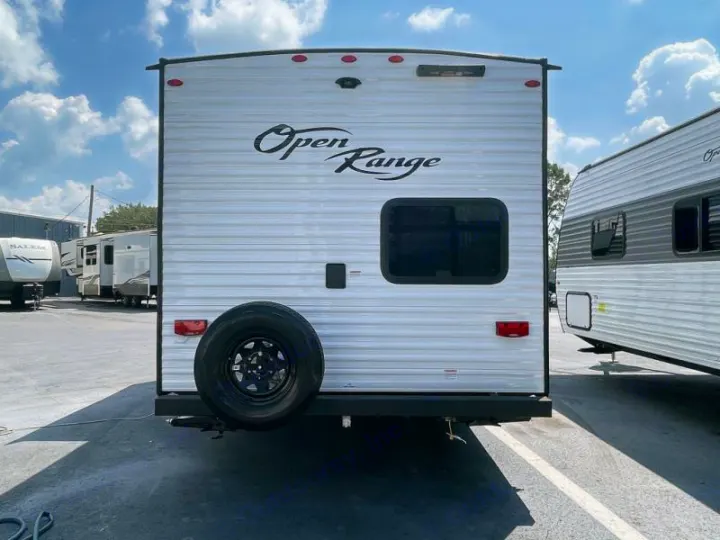 Rear view of a white Open Range travel trailer, featuring a spare tire and small window, perfect for an RV rental. Other RVs are visible in the background.. Open Range Colt MBS 18 2026