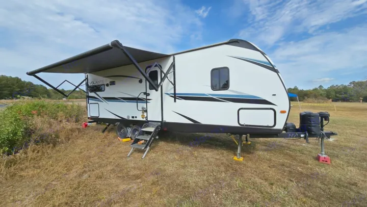 This rv rental, a modern travel trailer, is parked in a scenic grassy field with its awning extended for shade.. Crossroads RV Volante 2022