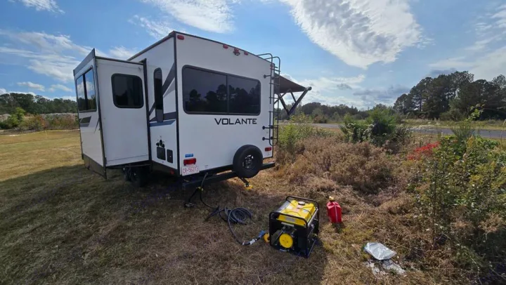 RV rental travel trailer parked in a sunny, grassy field with a generator and gas can nearby.. Crossroads RV Volante 2022