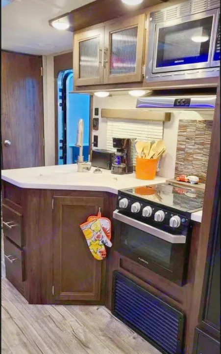This RV rental kitchen features dark wood cabinets, a white counter with a sink, microwave, stove, and coffee maker, ideal for travel.. Forest River Cherokee 2019