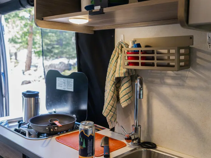 RV rental kitchen: compact stove, sink, and cooking area with outdoor views. Ready for adventure and meals on the road.. Winnebago Solis 2022