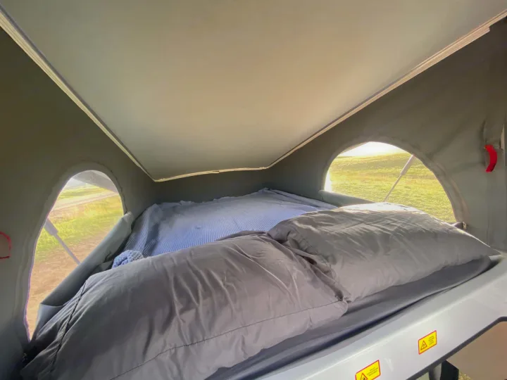 Cozy pop-top rv rental sleeping area with bedding, pillows, and outside views of a grassy field through side windows.. Winnebago Solis 2022
