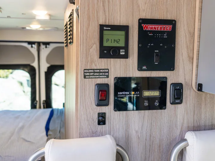An RV rental interior shows control panels: Truma heater, Winnebago system monitor (water, tanks), and Xantrex solar charger.. Winnebago Solis 2022