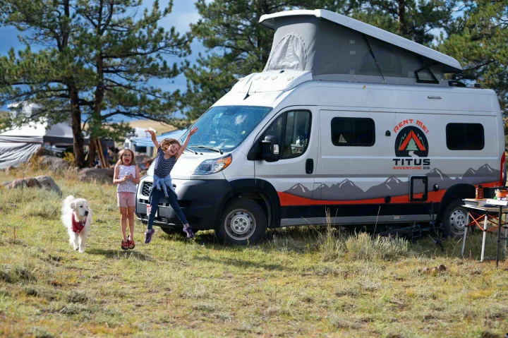 Two happy kids and a dog next to their pop-top RV rental from Titus Adventure Co. at a scenic campsite.. Winnebago Solis 2022