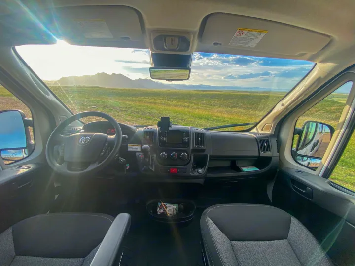 Inside an RV rental, dashboard view of a vast landscape, green fields, and distant mountains under a bright sky.. Winnebago Solis 2022