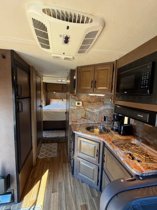 Inside a well-equipped rv rental featuring a kitchen with a sink, stove, microwave, coffee maker, toaster, and a cozy bedroom.. Thor Majestic 2019