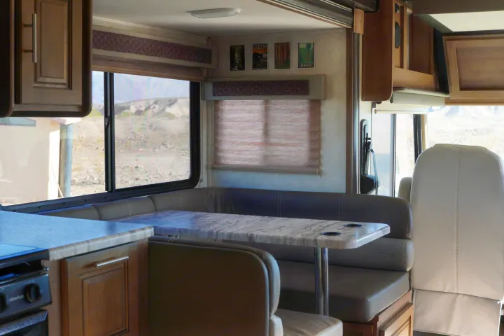 **RV rental interior** with a comfortable dining booth, table, kitchen, and window view of a rugged landscape.. FR3 FR3 Motorhome 2019