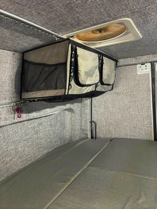 RV rental interior featuring practical overhead storage, a roof vent fan, and modular grey bed cushions for comfortable travel.. MERCEDES SPRINTER 144 2020