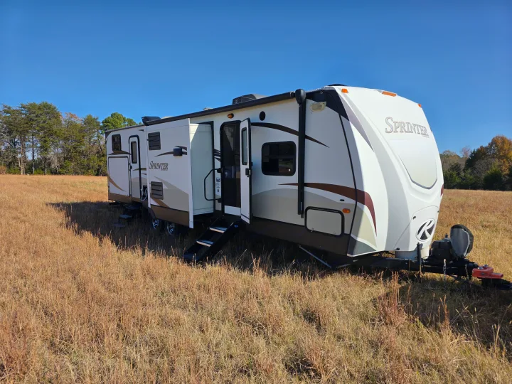 A white Sprinter RV with steps down and slide-outs extended, ideal for rv rental, in a sunny, dry grass field.. Keystone RV Sprinter 2013