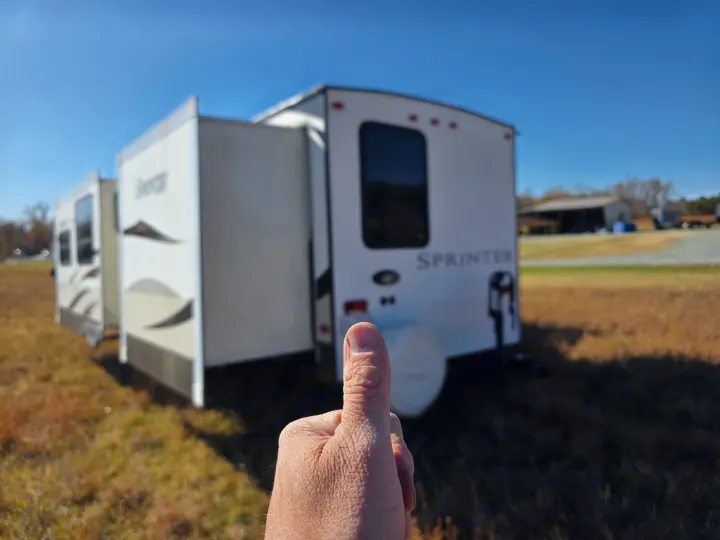 Thumbs-up for this RV rental! A white travel trailer with extended slide-outs stands ready in a sunny field under blue sky.. Keystone RV Sprinter 2013