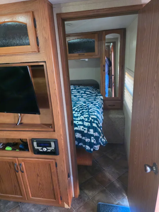 RV rental interior: bedroom with a bed, patterned blanket, mirrored closet, TV, and entertainment system.. Keystone RV Sprinter 2013