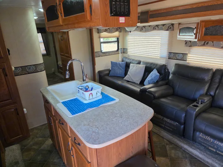 RV rental interior featuring a practical kitchen island, sink, and comfy leather sofa with a recliner. Ready for your trip!. Keystone RV Sprinter 2013