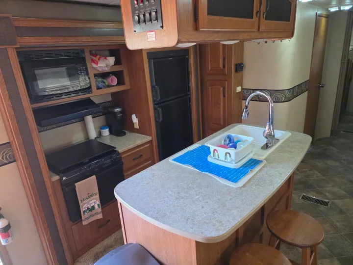 RV rental kitchen: Microwave, stove, fridge, and island with a sink, faucet, and dish drying rack.. Keystone RV Sprinter 2013
