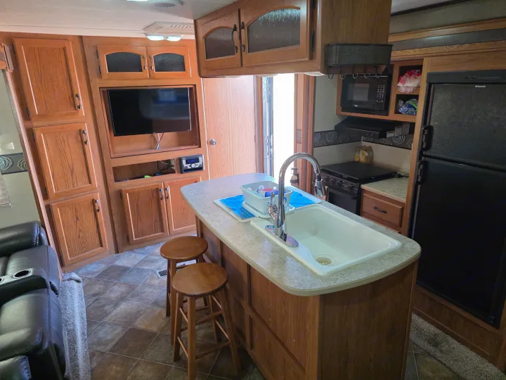 Cozy RV rental interior featuring a kitchen island with sink, stove, microwave, fridge, TV, and recliners.. Keystone RV Sprinter 2013