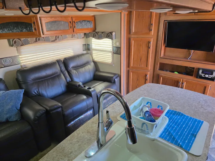 Step inside this RV rental featuring comfortable dark leather recliners, wooden cabinetry, a TV, and a kitchen sink.. Keystone RV Sprinter 2013
