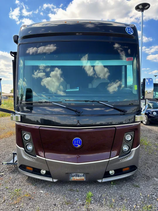 Striking front view of a dark brown and gray luxury motorhome. This HR-branded rv rental reflects the cloudy sky, parked on gravel.. Holiday Rambler Endeavor 2018