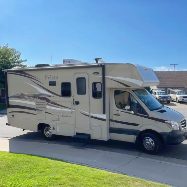 Experience adventure in this tan Coachmen Prism Class C motorhome, an ideal rv rental, parked on a sunny street.. Coachman Prism 2200 LE 2017
