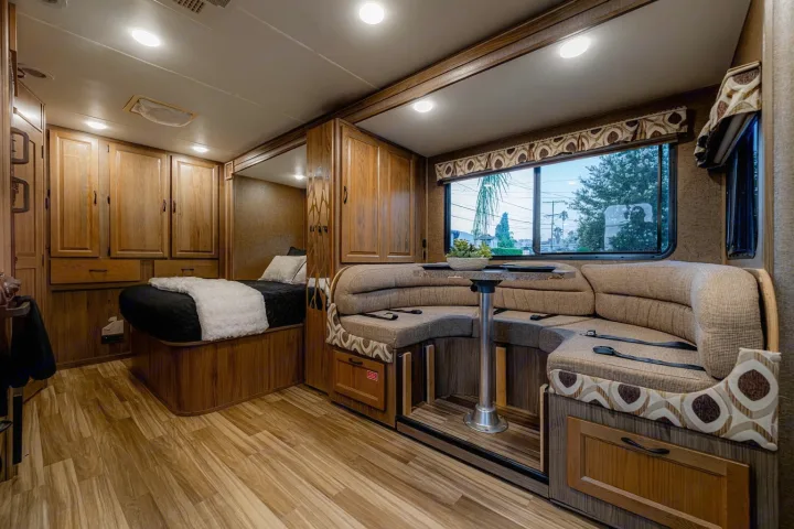 Spacious RV rental interior featuring a cozy bed, wooden cabinetry, and a comfy U-shaped dinette with a scenic window view.. Coachman Prism 2200 LE 2017